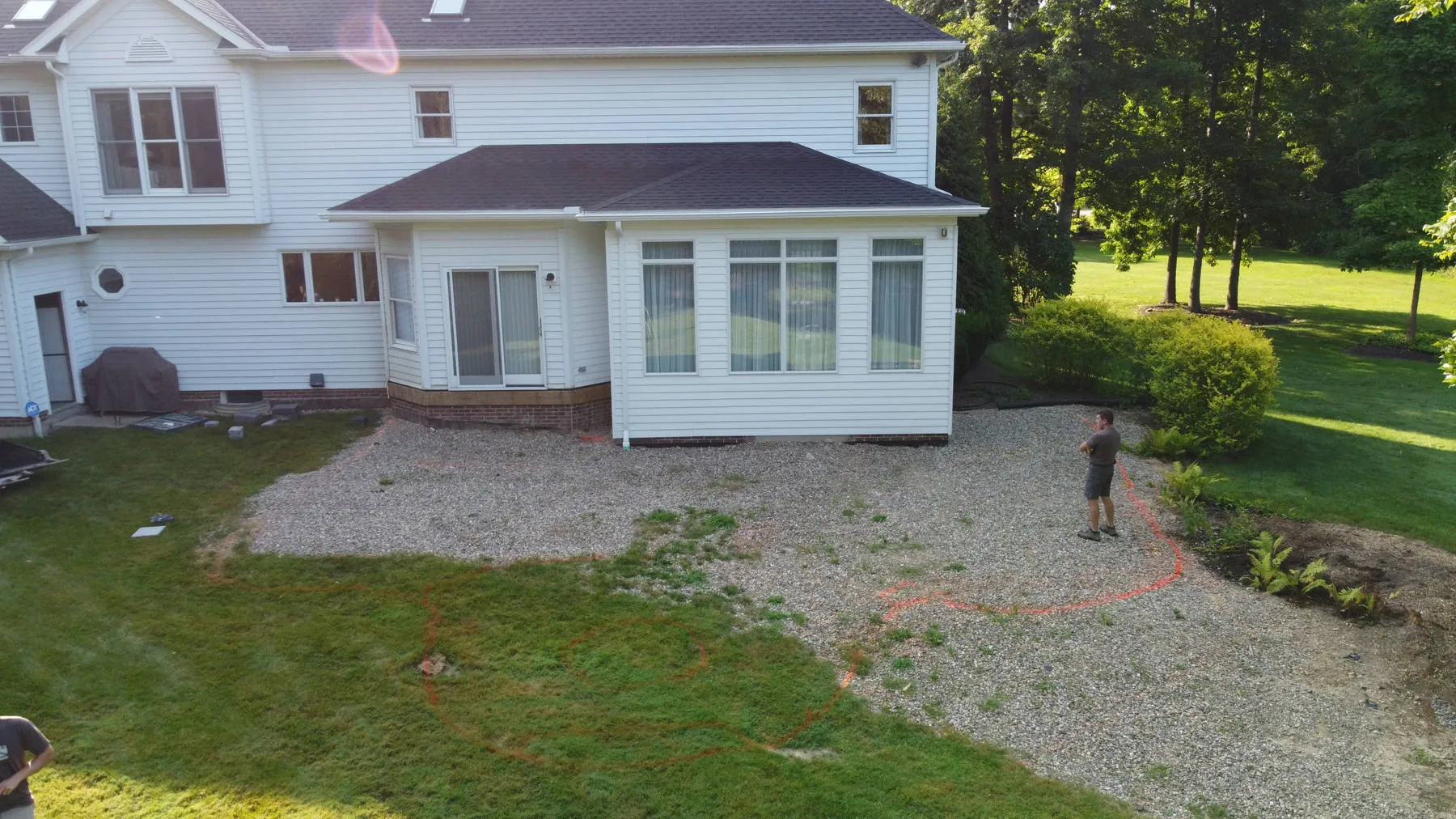 Before: a bare gravel pad with layout paint behind a white house with a sunroom, before the patio was built