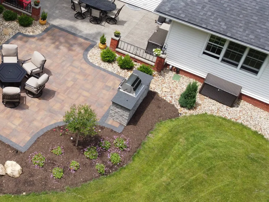 Built-in grill station with a stone-veneer base and a dark countertop at the corner of a paver patio with lounge chairs