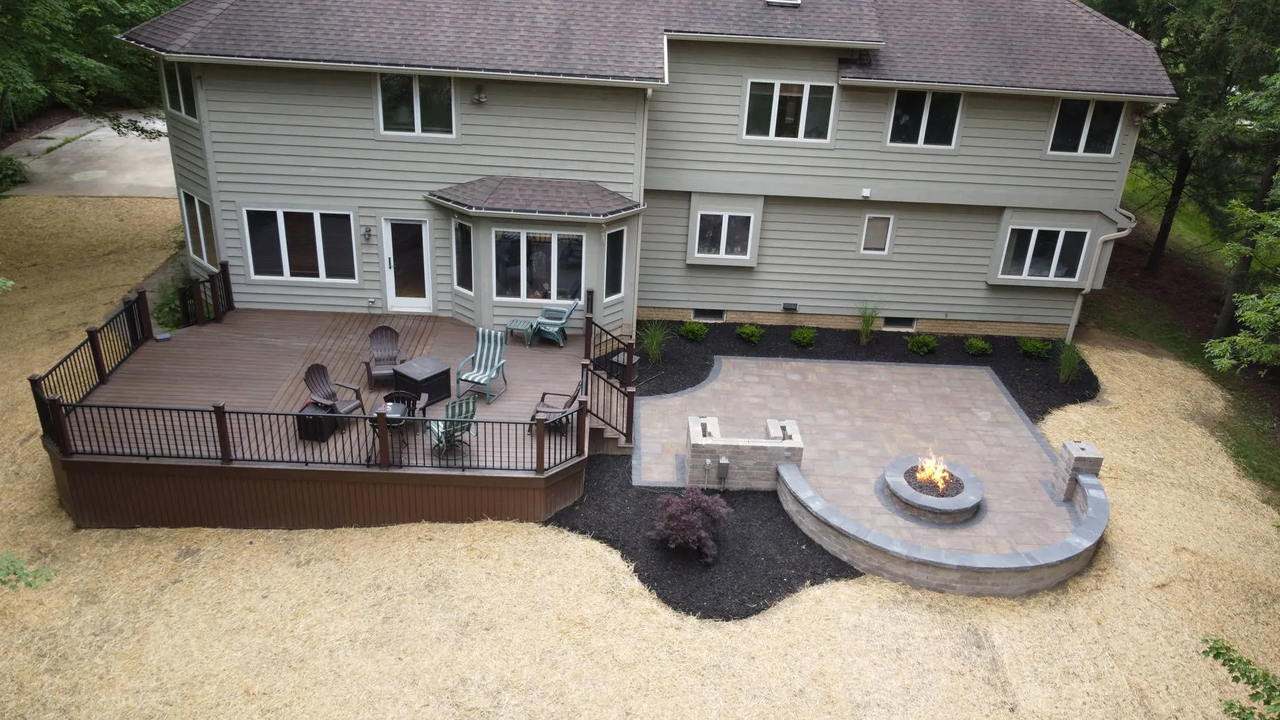 Just installed: a deck and paver patio with a lit fire pit and seat wall, with the new lawn still under straw
