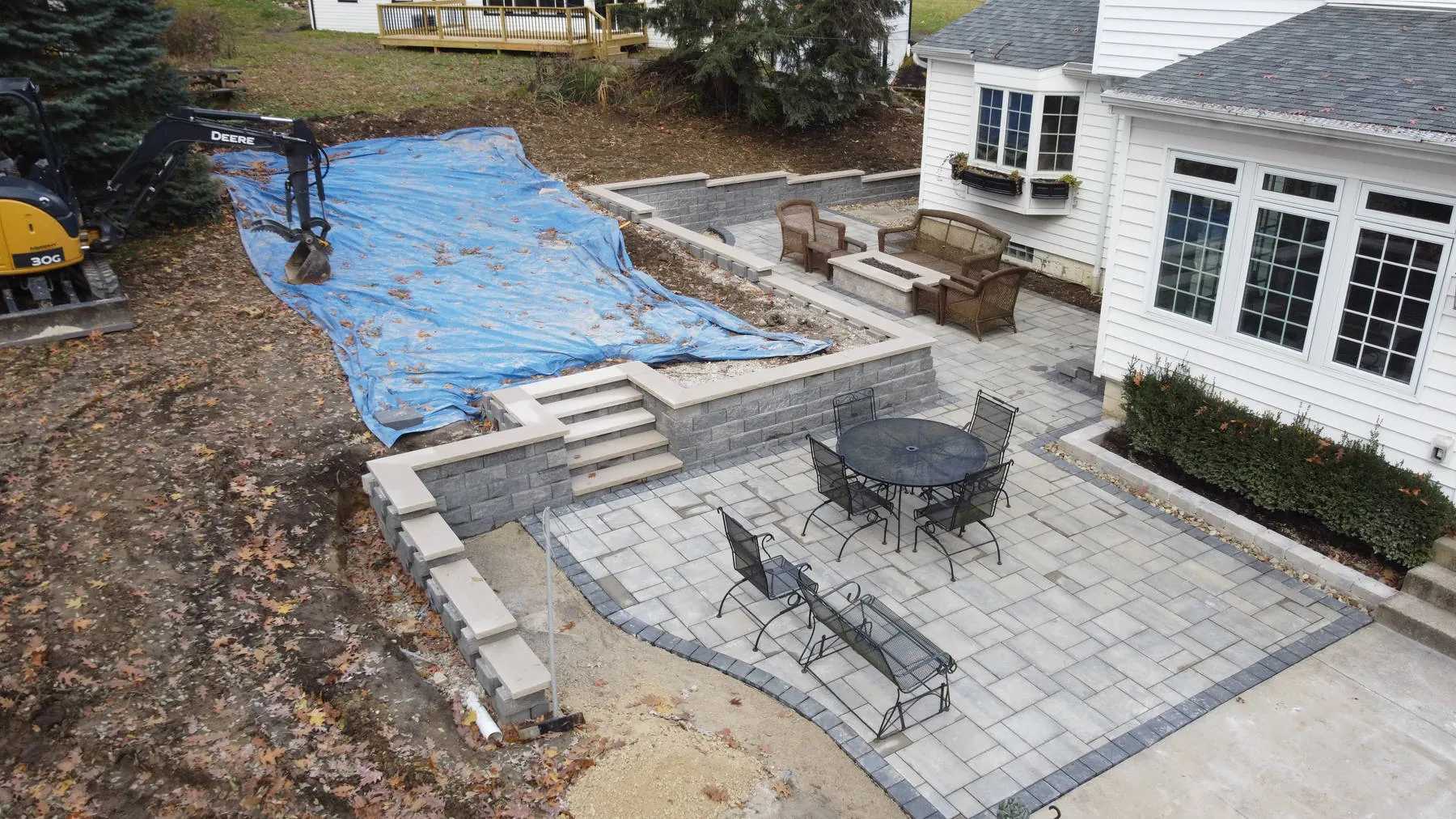 In progress: a finished paver patio and steps, with a blue tarp over the upper level and a mini excavator still on site