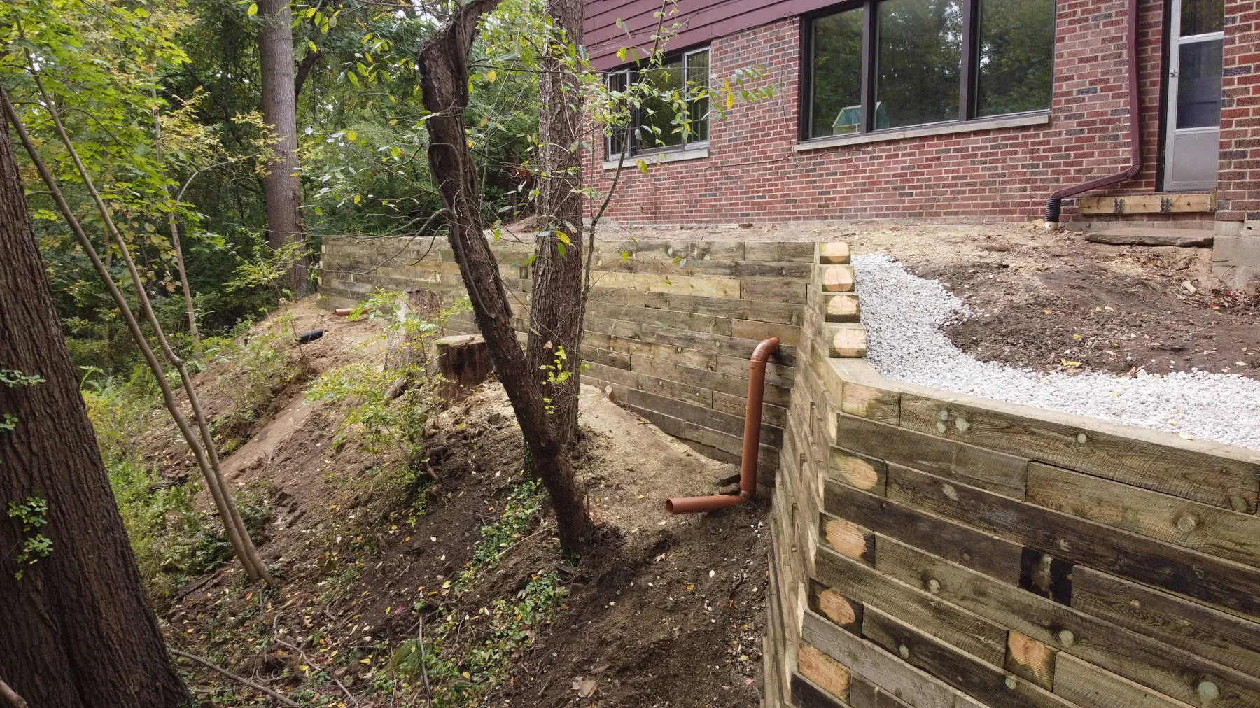 In progress: a partly built timber retaining wall on a wooded slope, with fresh gravel behind it